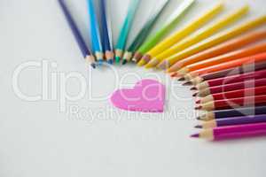 Colored pencils arranged in semi circle with heart on white background
