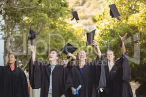 Successful graduate school kids throwing mortarboard in air in campus