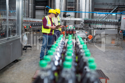 Two factory workers monitoring cold drink bottles on production line