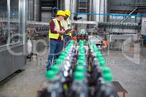 Two factory workers monitoring cold drink bottles on production line