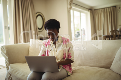 Woman sitting on sofa and using laptop in living room