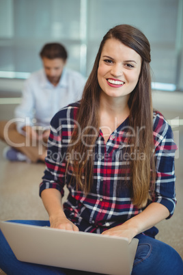 Portrait of female executive sitting on floor and using laptop