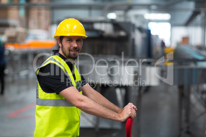 Smiling factory worker pulling trolley in factory