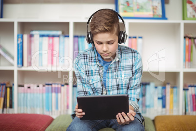 Attentive schoolboy listening music while using digital tablet in library
