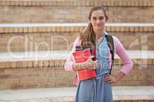Portrait of schoolgirl standing with schoolbag and books in campus