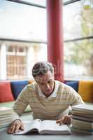 Attentive school teacher reading book in library