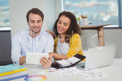 Smiling graphic designers sitting at table and using digital tablet