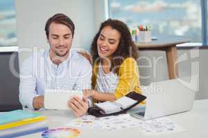 Smiling graphic designers sitting at table and using digital tablet