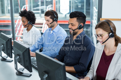 Business executives with headsets using computers at desk in office