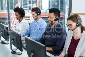 Business executives with headsets using computers at desk in office