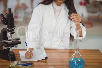 School girl writing in journal book while experimenting in laboratory