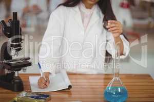 School girl writing in journal book while experimenting in laboratory