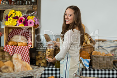 Portrait of smiling female staff holding a jar of cookies at counter