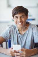 Portrait of happy schoolboy using mobile phone in classroom