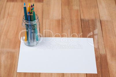 Jar of colored pencils kept on white paper