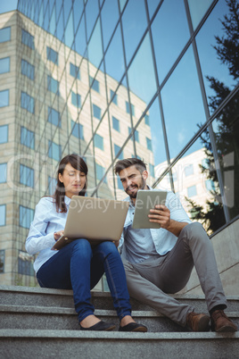 Executives using laptop and digital tablet outside office building