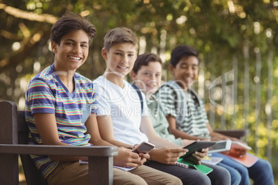 School kids using mobile phone and digital tablet on bench in school campus