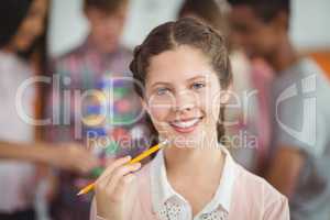 Portrait of smiling schoolgirl standing with pencil in classroom