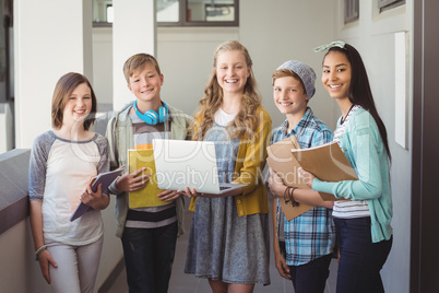 Portrait of smiling school students using laptop in corridor