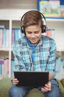 Happy schoolboy listening music while using digital tablet in library