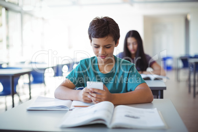 Schoolboy using mobile phone while studying in classroom Schoolboy using mobile phone while studying in classroom