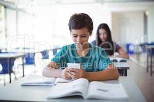 Schoolboy using mobile phone while studying in classroom