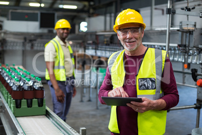 Smiling factory worker with digital tablet standing near the production line