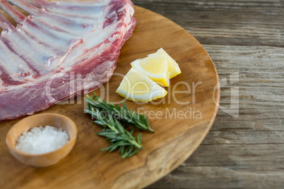 Beef ribs rack, rosemary herb, salt and lemon on wooden tray against wooden background
