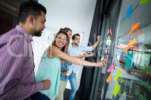 Business executives discussing over sticky notes on glass