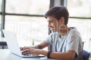 Happy schoolboy using laptop in classroom