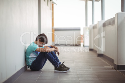 Sad schoolboy sitting in corridor