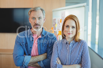 Portrait of male and female executives standing with arms crossed in conference room