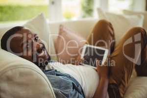 Man lying on sofa and using digital tablet