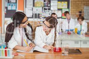 School girls writing in journal book while experimenting in laboratory at school