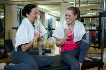 Happy women holding water bottle while relaxing after workout