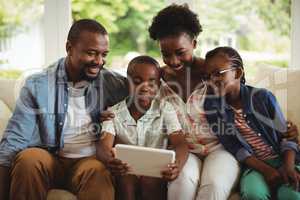 Parents and son using digital tablet on sofa in living room