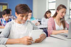 Students using digital tablet and laptop in classroom