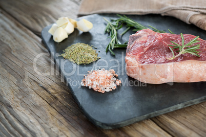 Sirloin chop and ingredients on slate board against wooden background