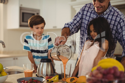 Father preparing smoothie with his kids in kitchen