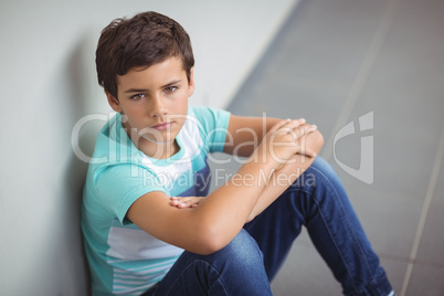 Portrait of sad schoolboy sitting in corridor