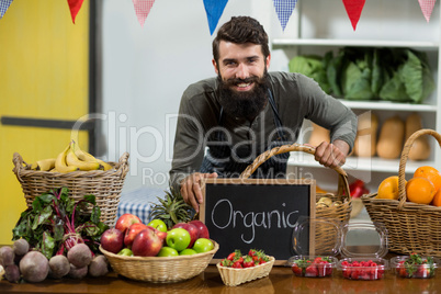 Smiling worker holding a board with organic sign at grocery store