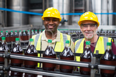 Smiling factory workers monitoring drinks production line