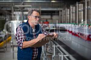 Male factory worker maintaining record on clipboard in factory