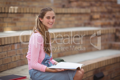 Portrait of schoolgirl reading book in campus