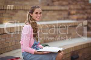 Portrait of schoolgirl reading book in campus