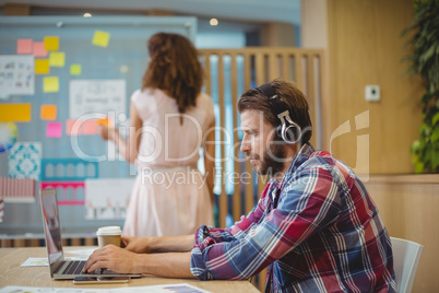 Male graphic designer listening song while using laptop