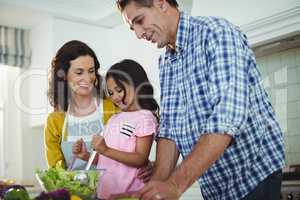 Parents and daughter preparing salad in kitchen