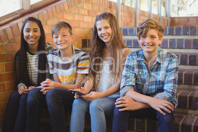 Smiling school students sitting on the staircase using mobile phone