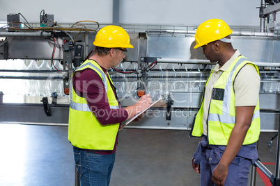 Two factory workers with clipboard working next to production line