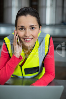 Female factory worker using laptop while talking on mobile phone